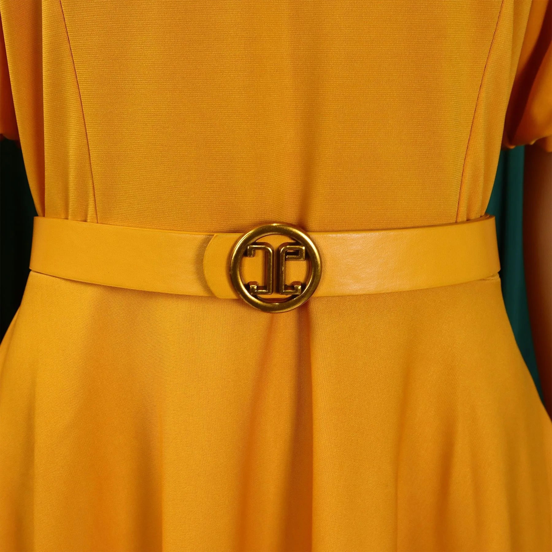 A mustard yellow pleated dress featuring a matching belt with a gold circular buckle.