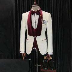 A white three-piece tuxedo featuring a burgundy velvet shawl lapel, vest, and matching bow tie.