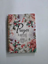 A spiral-bound prayer journal for women featuring a floral design on a wood-grain background.