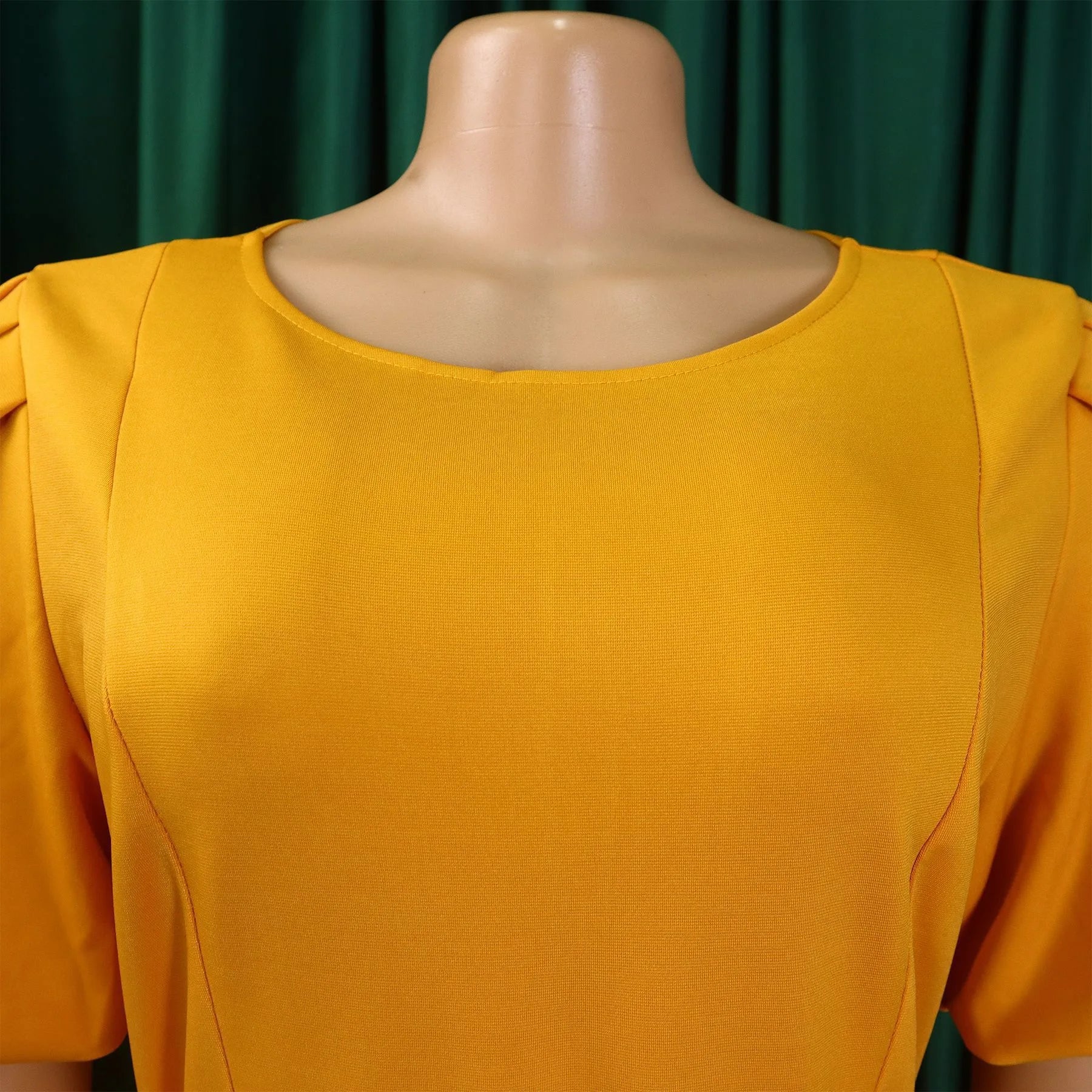 A mustard yellow short-sleeved dress with a round neckline on a mannequin.