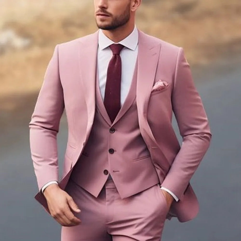 A man wears a dusty pink three-piece suit with a white shirt and a dark red tie.