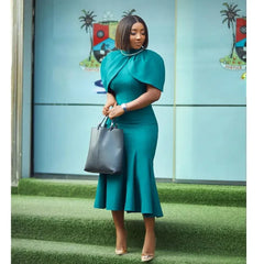 A woman wears a teal midi-length mermaid dress with a turtleneck and cape sleeves.