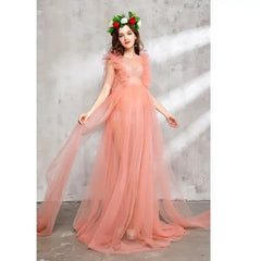 A pregnant woman wears a sleeveless, ankle-length peach tulle maternity dress with a floral crown.