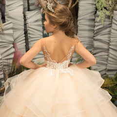 A girl wears a light champagne tulle ball gown with floral appliques and a tiered skirt.