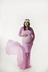 A pregnant woman wears a long-sleeved pink lace mermaid maternity gown with a floral headpiece.