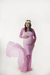A pregnant woman wears a long-sleeved pink lace mermaid maternity gown with a floral headpiece.