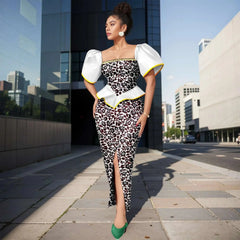 A woman wears an ankle-length Ankara print dress with white puff sleeves and a square neckline.