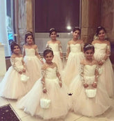 Seven young girls wearing matching champagne-colored lace ball gowns with long sleeves.