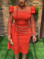 A woman wears a coral sheath dress with lace sleeves, beaded accents, and a side ruffle detail.