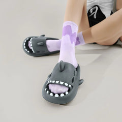 A person wears grey shark-shaped EVA slides with white teeth details over light purple socks.