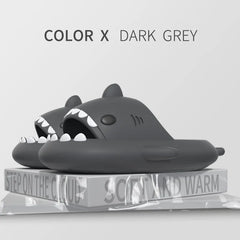 A pair of dark grey shark-shaped EVA slides resting on a block labeled soft and warm.