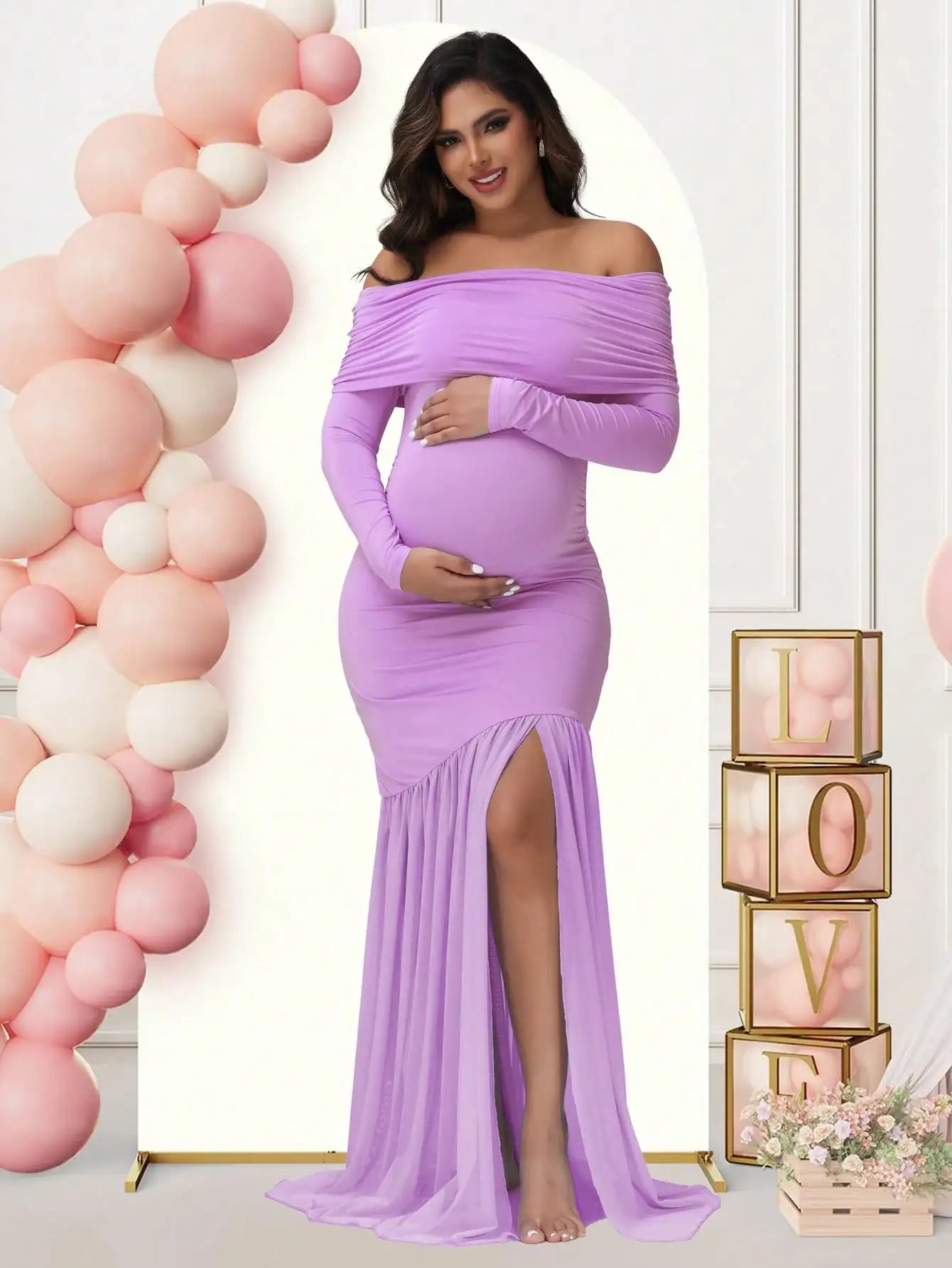 A pregnant woman wears a long-sleeved, off-shoulder lavender maternity gown with a side slit.