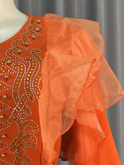 An orange dress featuring gold rhinestone embellishments and ruffled sheer sleeves.