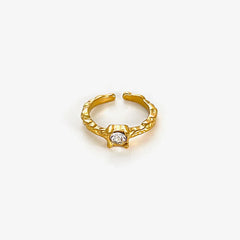 A gold-plated open ring featuring a textured band and a single central rhinestone setting.