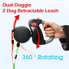 A hand holds a black dual retractable leash with two color-coded leads that rotate 360 degrees.
