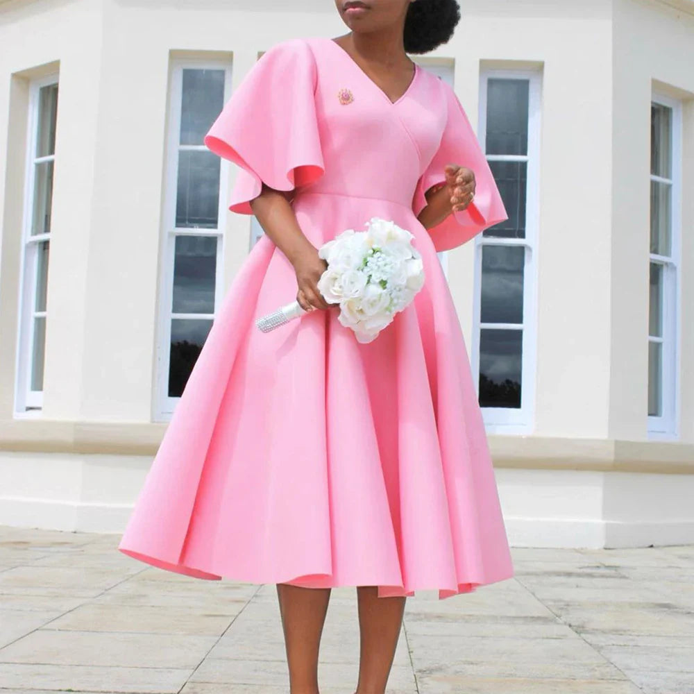 A woman wears a pink mid-calf A-line dress with a V-neck and butterfly sleeves.