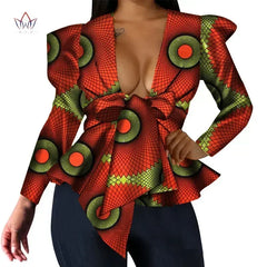 A woman wears a long-sleeved, V-neck top featuring a vibrant orange and green African print.