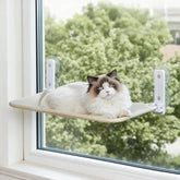 A fluffy cat rests on a beige fabric window perch secured to glass with four suction cups.