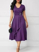 A woman wears a purple short-sleeve midi dress with a V-neck and an asymmetric ruffled hem.