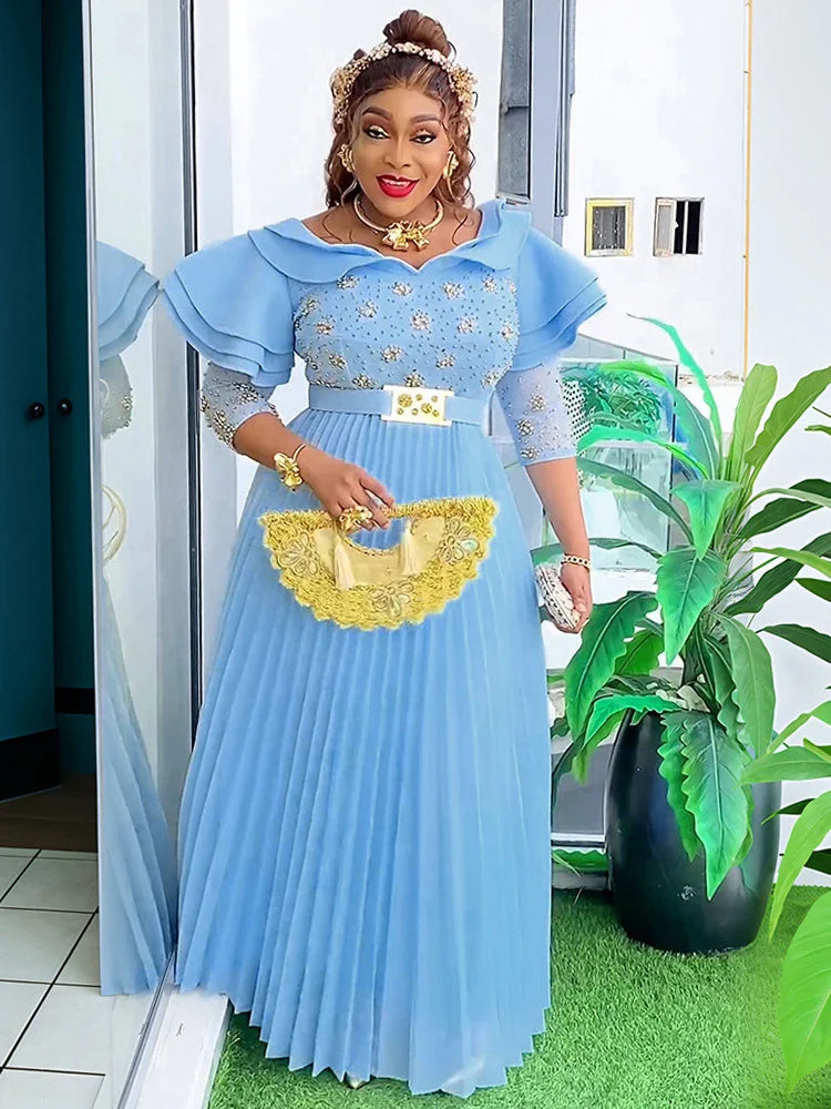 A woman wears a light blue floor-length pleated maxi dress with crystal embellishments and sleeves.