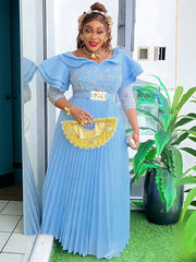 A woman wears a light blue floor-length pleated maxi dress with crystal embellishments and sleeves.