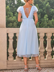 A woman wears a light blue, mid-calf length maternity dress with a V-neck and ruffled sleeves.