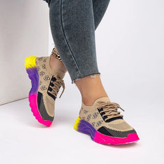A pair of beige and black knit sneakers with a vibrant yellow, purple, and pink gradient sole.