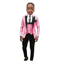 A boy wears a three-piece formal suit featuring a pink blazer, a pink vest, and black trousers.