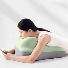 A woman rests on a green and grey wedge-shaped memory foam pillow while using a smartphone.