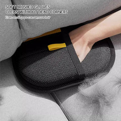 A hand wears a black mesh hair removal glove to clean pet fur from a grey sofa.