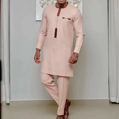 A man wears a light pink long-sleeve kaftan top and matching trousers with dark red trim.