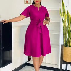 A woman wears a magenta knee-length A-line dress with short sleeves and a tie-waist belt.