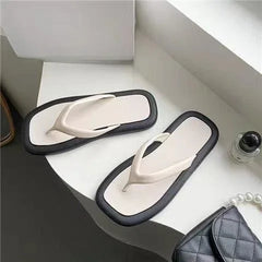 A pair of minimalist women's flip-flops featuring a cream-colored footbed and a black outer rim.