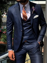 A man wears a dark blue three-piece slim-fit suit with a white shirt and orange striped tie.