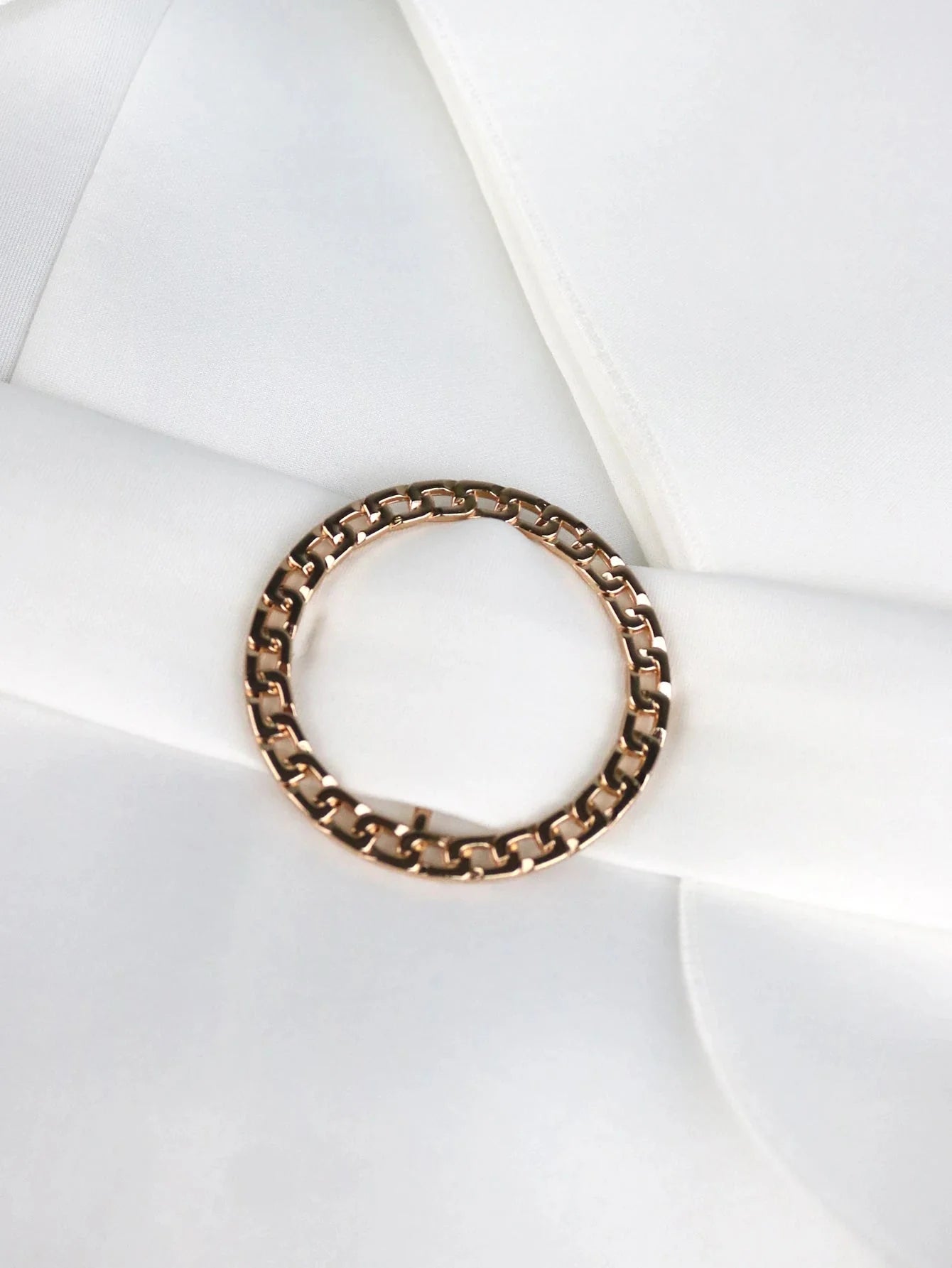 A rose gold chain link ring rests on a smooth white fabric surface.