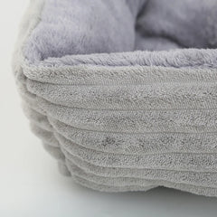 A close-up of a soft, grey, square pet bed with a ribbed exterior and plush interior lining.