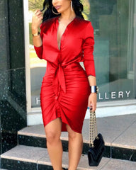 A woman wears a red long-sleeve bodycon dress with a deep V-neck and a front tie detail.