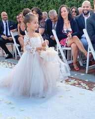 A young girl wears a floor-length, long-sleeved lace and tulle ball gown at a wedding.