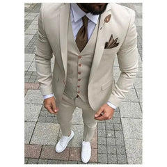 A man wears a slim-fit beige three-piece suit with a brown tie and white sneakers.