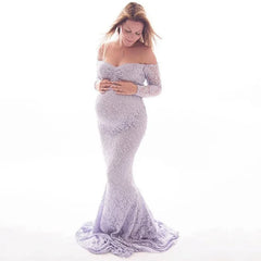 A pregnant woman wears a long-sleeved, off-the-shoulder lavender lace mermaid maternity gown.