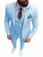 A man wears a light blue three-piece slim fit suit with a brown tie and white sneakers.