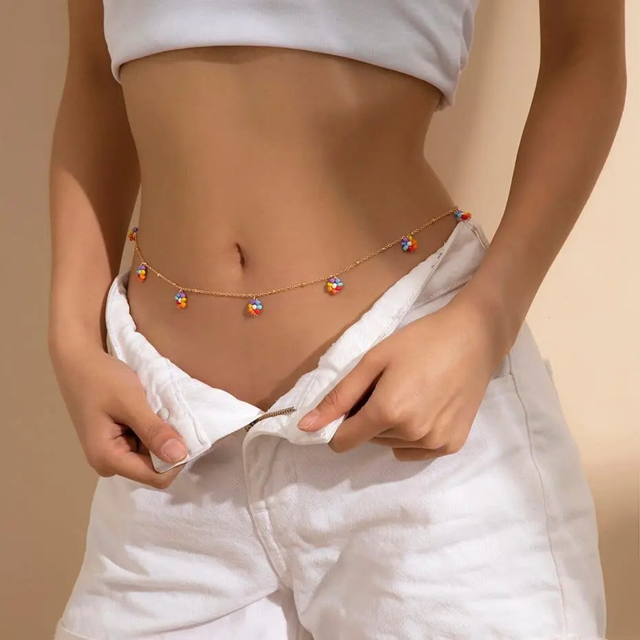 A woman stands against a neutral background with her hands in her white pants, wearing a crop top and accessorizing with the Sexy Vintage Aesthetic Belly Chain Thin Beads Link Body Chain Waist Chain Belt Y2K Streetwear.