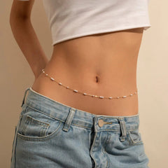 Wearing a white crop top and light blue jeans, a person highlights their look with the Sexy Vintage Aesthetic Belly Chain, a thin beaded Y2K streetwear waist chain that adds fashionable summer body jewelry flair.