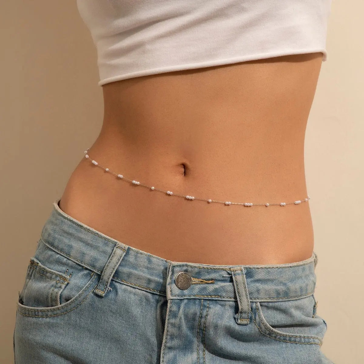 A woman in blue jeans and a white crop top highlights the Sexy Vintage Aesthetic Belly Chain Thin Beads Link Body Chain—trendy Y2K summer body jewelry perfect for stylish streetwear looks.