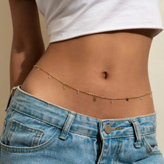A close-up of a person’s midriff wearing light blue jeans, a white crop top, and the Sexy Vintage Aesthetic Belly Chain Thin Beads Link Body Chain Waist Chain Belt, highlighting trendy Y2K summer fashion jewelry.