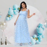 A pregnant woman wears a light blue, sleeveless, ankle-length tulle dress with floral embroidery.