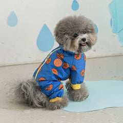 A small grey dog wears a blue hooded, four-legged waterproof raincoat with a brown pattern.