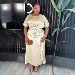 A woman wears a champagne-colored satin midi dress featuring short sleeves and a floral waist detail.