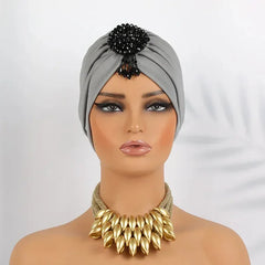 A grey pleated turban headscarf featuring a black beaded embellishment on the front.
