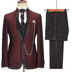 A three-piece burgundy floral jacquard suit with a stand collar, black vest, and matching trousers.